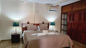 Habitación de hotel con cama, dos lámparas de noche, mesita de noche, equipo de aire acondicionado y armario de madera.