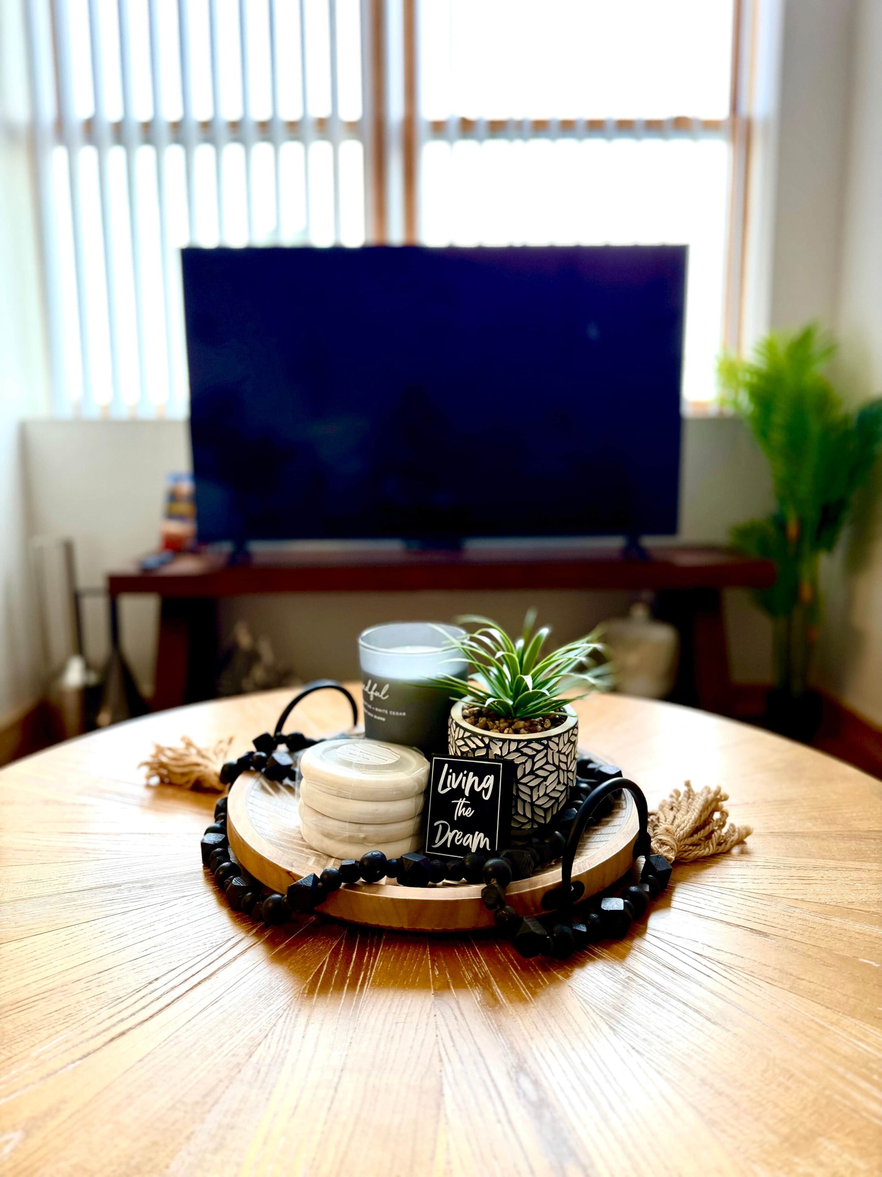A wooden table with a tray holding candles, a small potted plant, and a sign that reads 'Living the Dream.'
