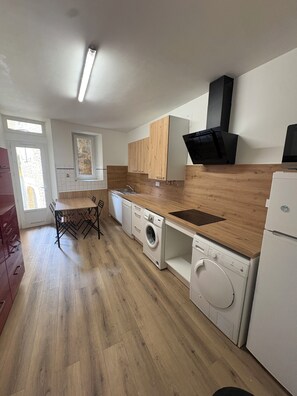 A modern kitchen with wooden cabinets, a built-in oven, a washing machine, and a dining area with a table and chairs. - La Comtoise du Barry, medieval center of Sarlat. (Sarlat-la-Canéda)
