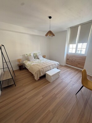 A bedroom with a bed, bedside tables, a hanging light fixture, a bench, a chair, and a window with blinds. - La Comtoise du Barry, medieval center of Sarlat. (Sarlat-la-Canéda)
