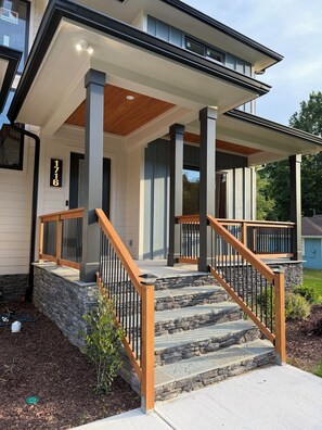 Ein modernes Haus mit überdachter Veranda, Steinstufen und einem Holzgeländer.