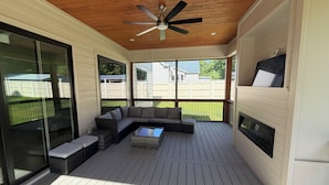 Eine überdachte Terrasse mit Deckenventilator, einem Ecksofa und einem Kamin.