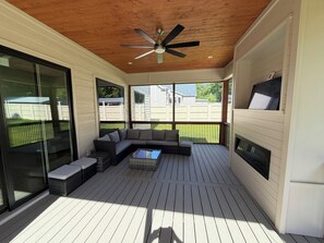 Eine überdachte Terrasse mit Deckenventilator, einem Ecksofa und einem Kamin.