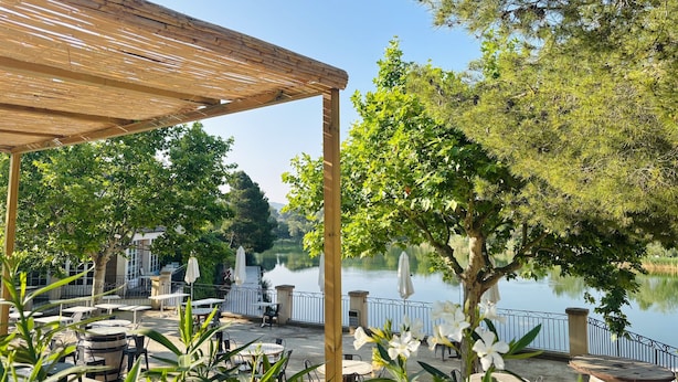 An outdoor patio with tables and chairs, a wooden pergola, and a lake view. - Chic Riverfront Stay With Terrace (Mallemort)