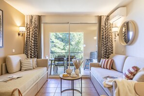 A modern living room with a sofa, a small table with decorative items, and a balcony with a view of trees.