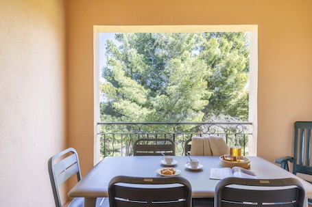 A balcony with a table set for two, a view of trees, and a metal railing.. Chic Riverfront Stay With Terrace