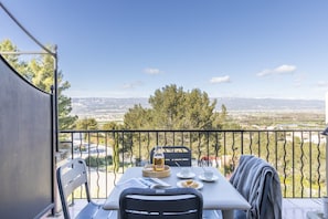 Un balcon avec une table dressée pour deux personnes, une chaise et une vue sur une vallée.