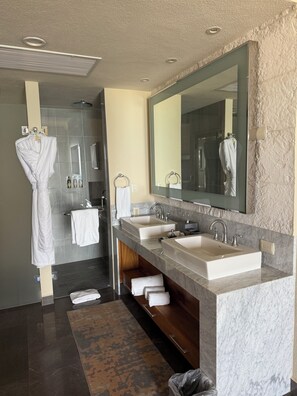 Un baño moderno con un espejo grande, dos lavamanos, una ducha y un perchero para bata.