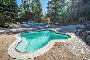 A swimming pool with a unique shape, surrounded by a paved area and trees. - Charming Alpine Getaway at St. Anton 661 (Mammoth Lakes)