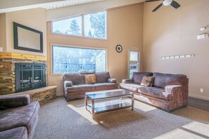 A living room with a fireplace, two sofas, a coffee table, and large windows. - Charming Alpine Getaway at St. Anton 661 (Mammoth Lakes)