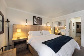 A hotel room with a large bed, bedside tables with lamps, a wooden headboard, and a mirror. - Charming Alpine Getaway at St. Anton 661 (Mammoth Lakes)