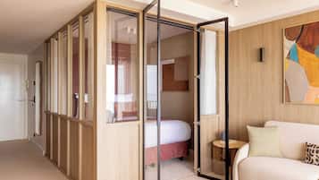 A modern hotel room with a sliding closet, a bed, a sofa, and a painting on the wall.