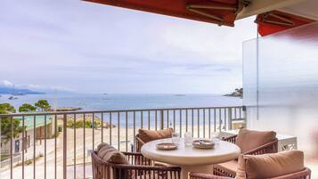 A balcony with wicker furniture, a round table, and a view of the sea and beach.
