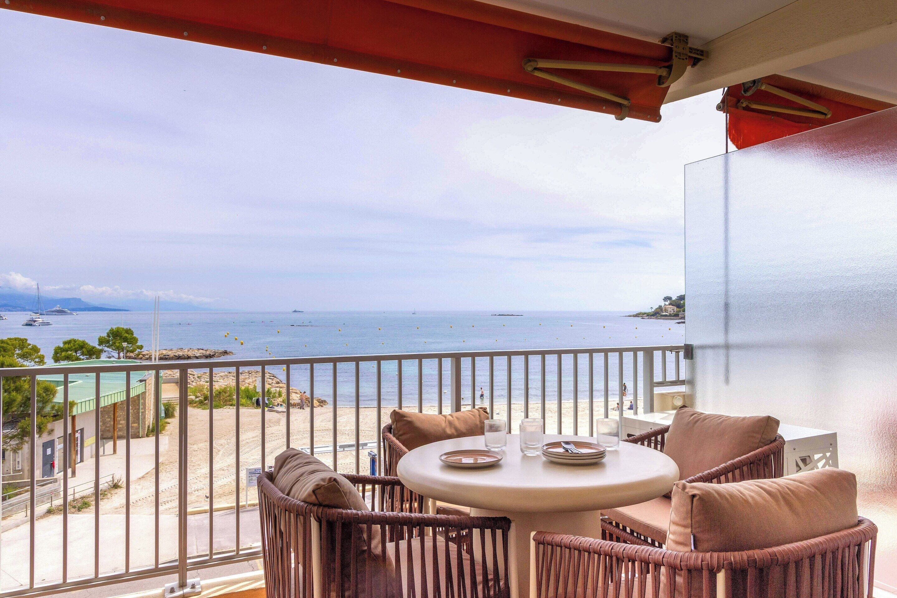 A balcony with wicker furniture, a round table, and a view of the sea.