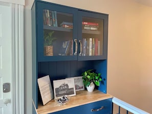 A blue bookcase with glass doors, a small white vase with a plant, and a framed picture on a wooden shelf.