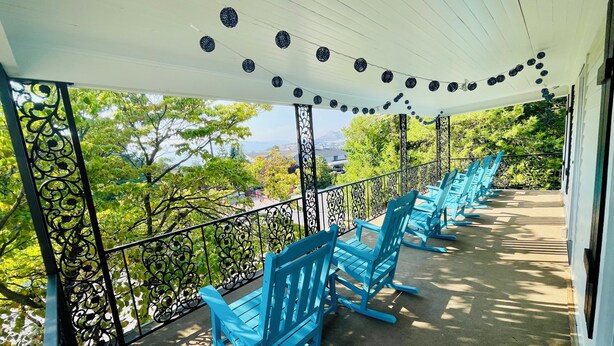 A covered outdoor seating area with blue chairs, a white ceiling, and a view of trees and buildings. - Walk to Lake & Downtown Chelan! Room #5 (Chelan)