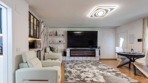 A modern living room with a flat-screen TV, a fireplace, a dining area with a table and chairs, and a sofa. - Family-friendly Calpe Home With Pool (Calpe)