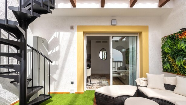 A modern outdoor living area with a spiral staircase, a seating area with cushions, and a green artificial turf. - Family-friendly Calpe Home With Pool (Calpe)