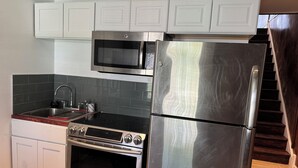 Una cocina con gabinetes blancos, un refrigerador de acero inoxidable, un microondas, una estufa y un lavamanos.