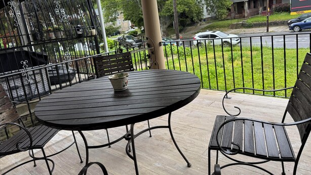 Un patio con una mesa redonda y dos sillas, baranda de metal, y vistas a la calle y casas.