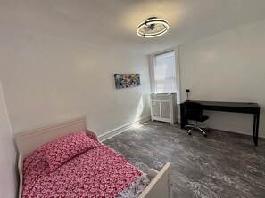 Une chambre Ă coucher avec un lit, un bureau, un radiateur et un ventilateur de plafond.