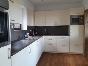 Eine moderne Küche mit weißen Schränken, einer Edelstahl-Spüle, einer Mikrowelle und einer Kaffeemaschine.