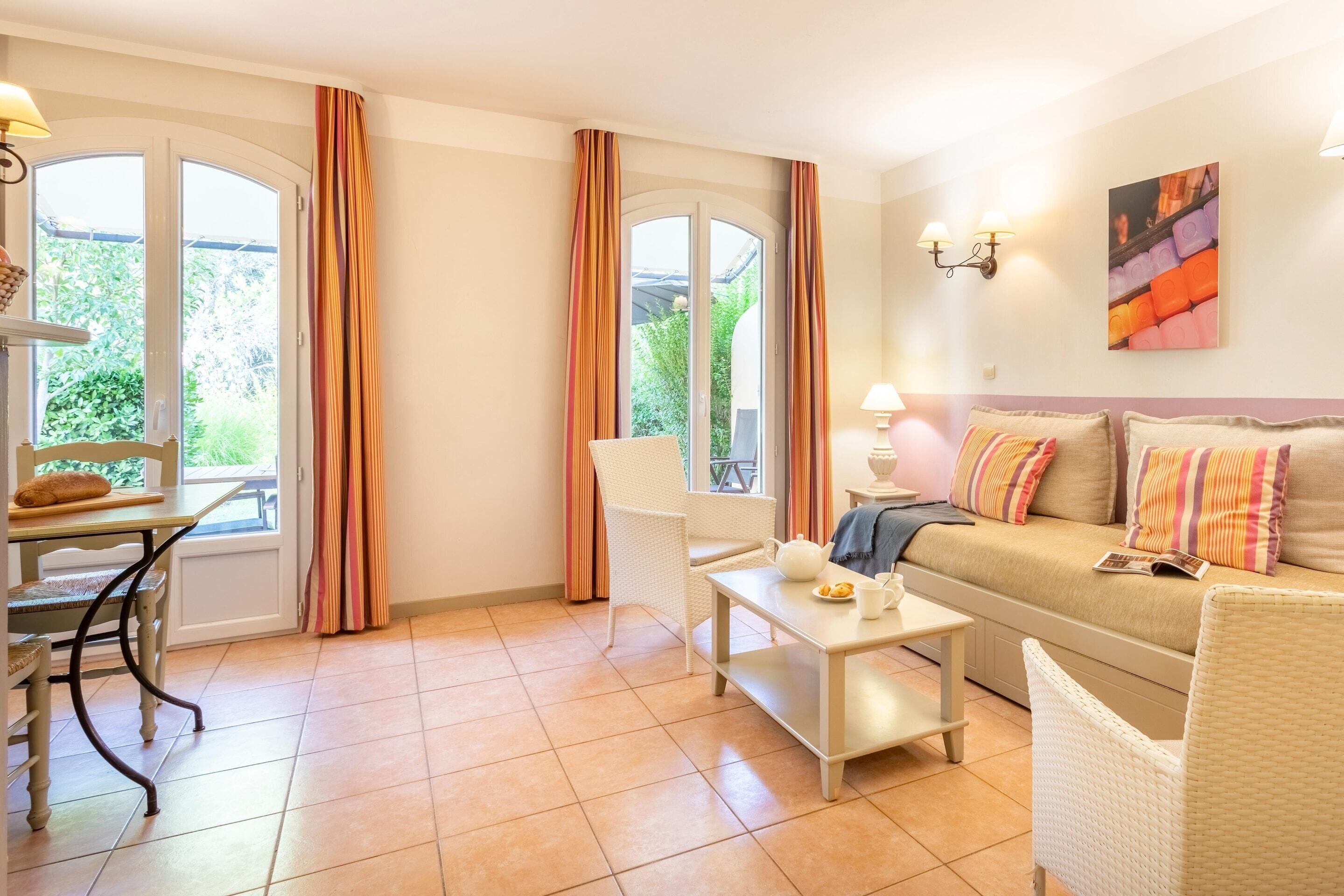 Ein gemütliches Zimmer mit einer Couch, einem Esstisch, einem Stuhl und einem Fenster mit Vorhängen.