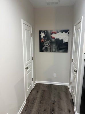 A hallway with two white doors, a dark wooden floor, and a large abstract painting on the wall. - Comfortable 3-bedroom townhome in beautiful East Point with AC & amenities (East Point)