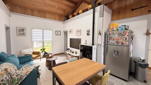 Ein moderner Wohnraum mit Holzboden, einer Couch, einem Esstisch, einem Fernseher und einem Kühlschrank.