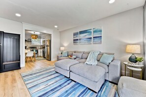 A modern living room with a grey sofa, a striped rug, and a kitchen in the background. - Beachside family getaway just steps from the sand. (Jacksonville Beach)