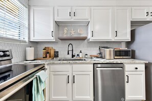 A modern kitchen with white cabinets, a stainless steel dishwasher, a microwave, and a stove. - Beachside family getaway just steps from the sand. (Jacksonville Beach)