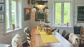 Une salle à manger avec une table en bois, des chaises, un lustre et une vue sur la verdure à l’extérieur.
