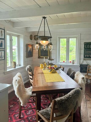 A dining room with a wooden table, chairs, a chandelier, and a view of greenery outside.