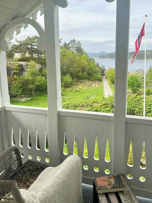 A porch with a view of a lake, greenery, and a flag.