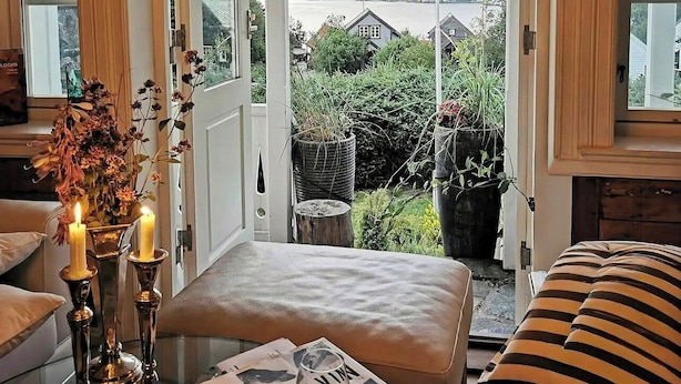 Ein Zimmer mit Seeblick, eine Bank, ein Tisch mit Kerze und ein Fenster mit Vorhang.