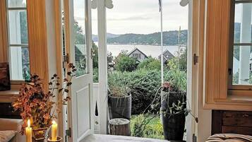 Une pièce avec vue sur un lac, un banc, une table avec une bougie et une fenêtre avec un rideau.
