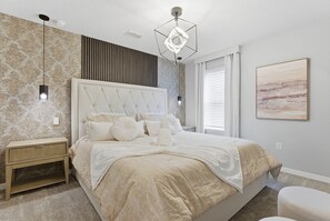 Et soveværelse med en polstret sengegavl, et natbord, en hængende lampe og et vindue med persienner.