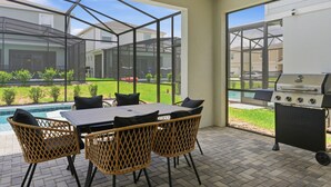 Une terrasse extérieure avec une table et des chaises, un barbecue et une vue sur une piscine et un espace verdoyant.