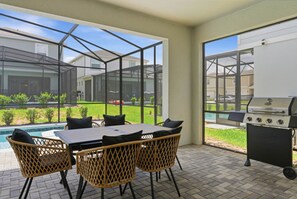 Eine Terrasse im Freien mit Tisch, Stühlen, einem Grill und Blick auf einen Pool und Grünflächen.