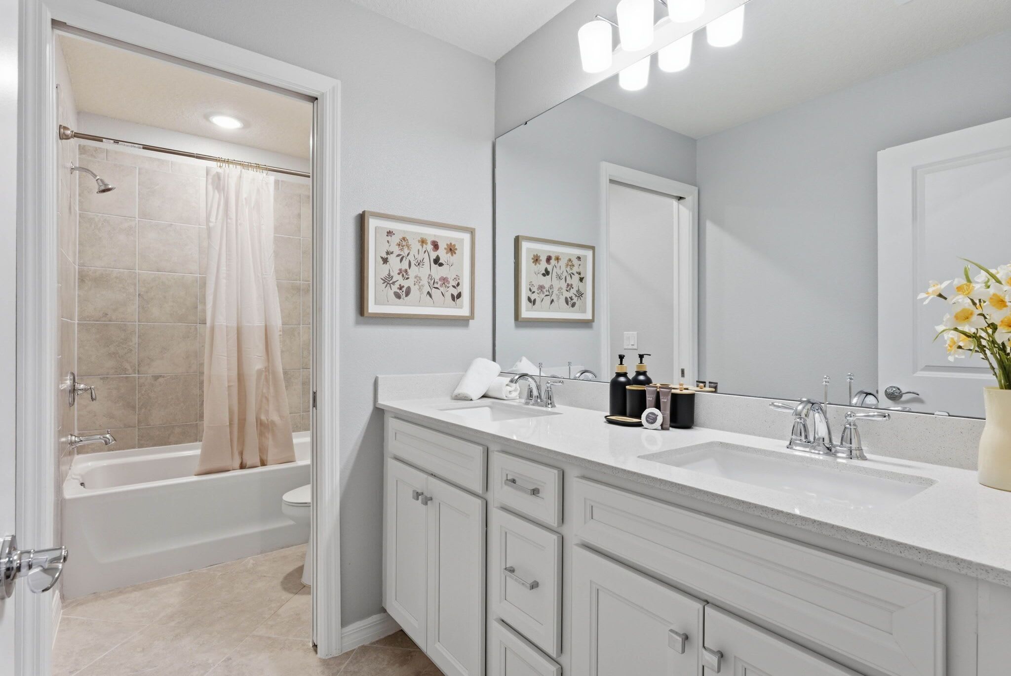 A bathroom with a bathtub, toilet, vanity with a mirror, and framed floral artwork.
