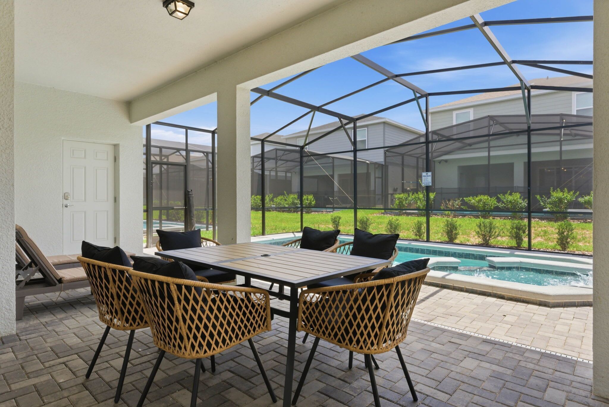 A covered patio with a table and chairs, a swimming pool, and a view of a house through a glass enclosure.