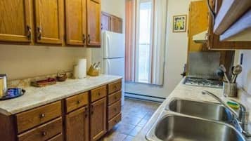A kitchen with wooden cabinets, a refrigerator, a sink, and a window with curtains.