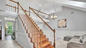 A staircase with wooden steps and white balusters, a chandelier, a gray sectional sofa, and a large floral artwork on the wall.