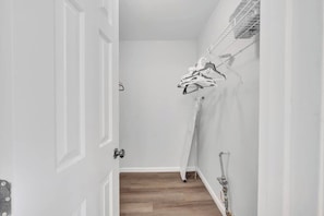 Un pasillo con una puerta blanca, un perchero de metal con ropa y una zona de ducha.