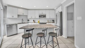 A modern kitchen with white cabinets, a granite countertop, and three bar stools.