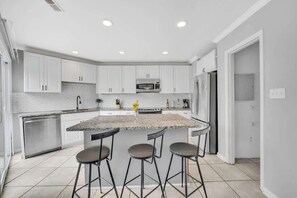 Une cuisine moderne avec des meubles blancs, un plan de travail en granit et trois tabourets de bar.