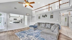 A spacious living room with a grey sofa, a blue patterned rug, and a ceiling fan.