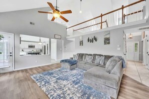 Un salon spacieux avec un canapé gris, un tapis à motifs bleus et un ventilateur de plafond.