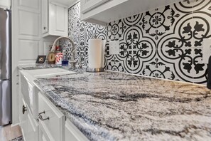 A kitchen with white cabinets, a granite countertop, and black and white patterned backsplash.