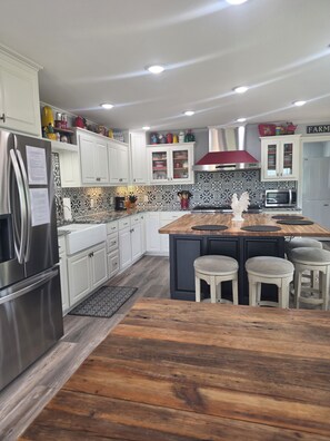 A modern kitchen with white cabinets, a wooden island, stainless steel appliances, and a patterned backsplash.
